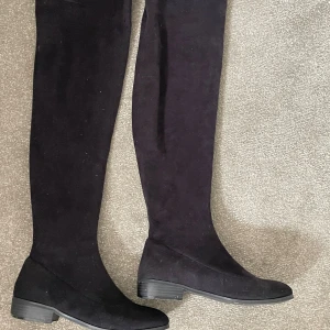 Svarta overknee boots - Ett par svarta stövlar med låg klack. Skorna har en enkel och elegant design som passar perfekt för höst- och vintermånaderna. dom är lite dammiga men har inga skador. passar 36/37