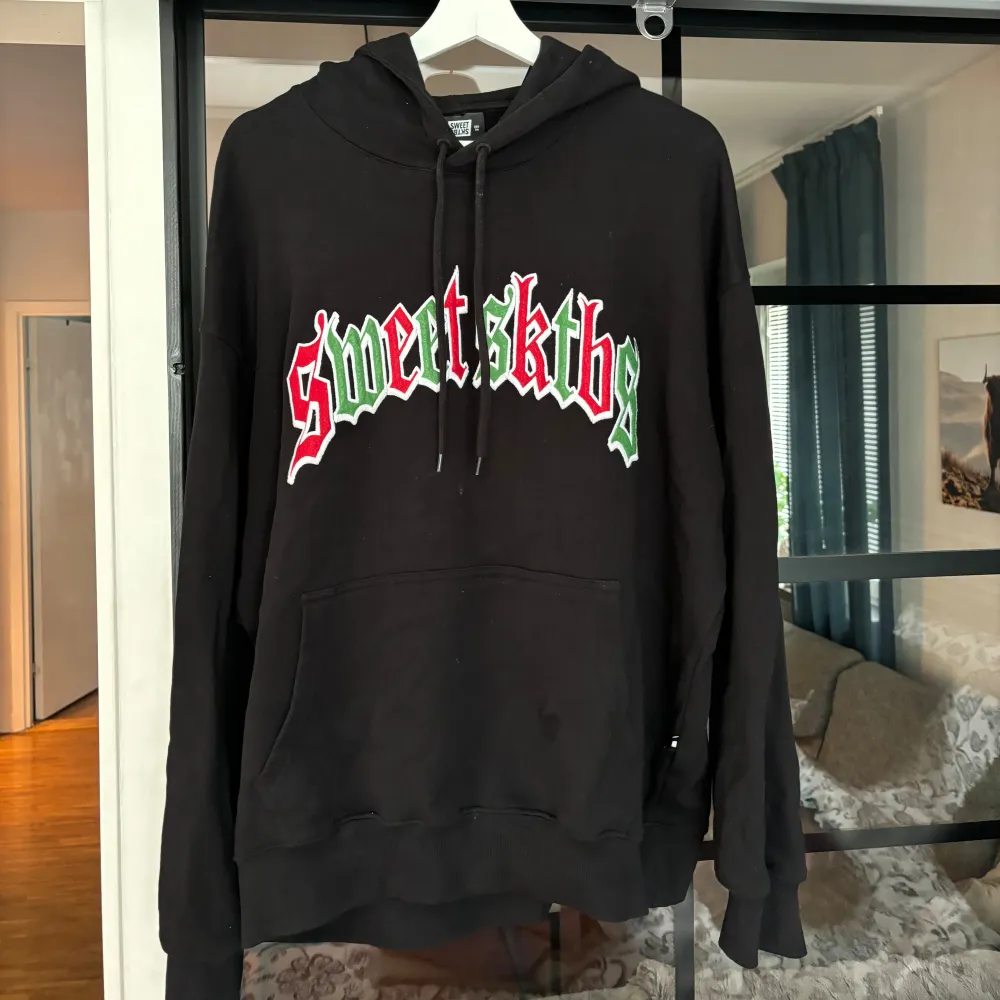 En svart hoodie från Sweet SKTBS med ett färgglatt tryck i rött, vitt och grönt på bröstet. Hoodien är i storlek M och kostar 699kr nypris . Hoodies.