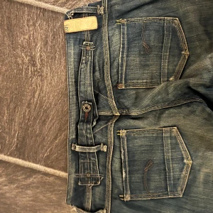 Lågmidjade vintage jeans - Hej, jag säljer nu dessa väldigt fina vintage jeans eftersom de har blivit försmå. De är i storlek 34 och har detaljer både där fram och där bak och ett hål på ena knät.