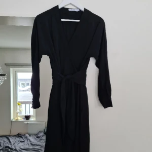 Svart långklänning  - Svart långklänning, omlott, v-ringad. Det följer med en extraknapp. Använd 1 gång, nyskick och normal i storleken. Kom med prisförslag😊  Material: 100% Polyester. 