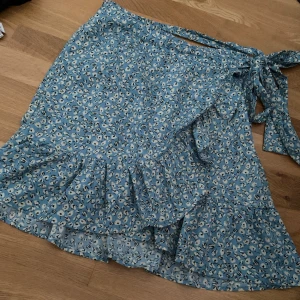 Blå kjol - Säljer denna blåa kjol med mönster då jag inte använder längre, den är i väldigt bra skick. Storlek M från Only. Finns en rosett som man kan knyta efter sin midja. Ordinarie pris 280kr.  