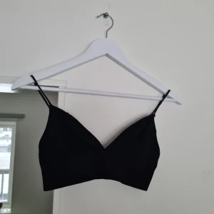 Svart topp - Svart topp med smala axelband. Skönt att ha när man bara ska vara hemma eller inte orkar ha på sig en bh men ändå vill ha stödet. Knappt använd. Det står storlek M men är mer som en S.  Material: 96% Återvunnen Polyamid, 4% Elastan.