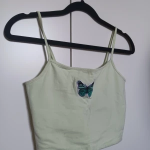 Grön croptop - En grön croptop med en fjäril framtill.  Mycket mer pastelgrön än vad som framgår på bilden. Superfin och skön att ha på sig. Säljer pga använder inte.   Köparen står för frakt 💕