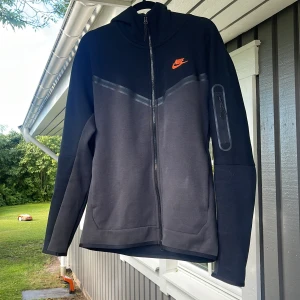 Techfleece strl M - En dress från Nike i nyskick! Den är i strl M. Mörkgrå och svart med orange logga