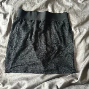 Svart kjol med spetsdetaljer - En elegant svart kjol med spetsdetaljer. Kjolen har en elastisk midja för en bekväm passform.