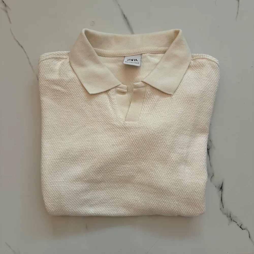 En stilren beige pikétröja från Zara. Tröjan har korta ärmar och en klassisk krage med knappslå. Materialet är bekvämt och passar perfekt för både vardag och avslappnade tillfällen.. T-shirts.