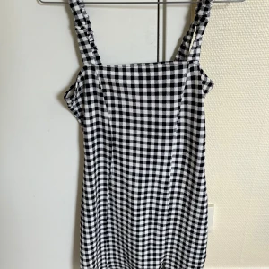 Svart och vit rutig klänning - En svart och vit rutig klänning med smala axelband. Klänningen har en rak passform och är ärmlös. aldrig använd 