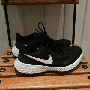 Ett par svarta Nike revolution skor med en vit Nike symbol på sidan, storlek 36,5. Använda 2 gånger därmed inget slitage☺️