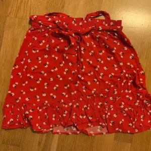 En röd blommig kjol i barnstorlek 158/164. Kan eventuellt passa som XXS/XS också!