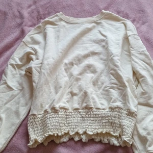 Vit tröja strl M - En krämvit tröja med en mudd längst ner som sitter bekvämt imot kroppen. Jättefin och väldigt lite använd