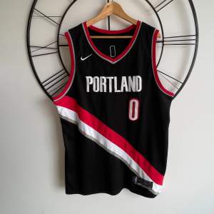 Jersey/Basketlinne för NBA-laget Portland Trail Blazers. Spelaren Damian Lillard på ryggen (#0). Storleken är L och linnet sitter bra på mig som är 1,85 och något bredaxlad. Gott skick. 