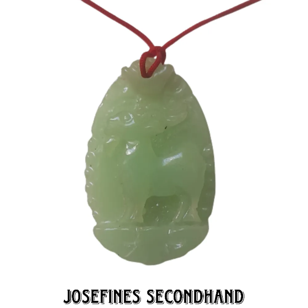 Halsband med jade sten och rött snöre med motiv av en get. Har liten jade sten som används för att justera storleken på halsbandet. Skickas med brev, frakt blir 15 kr. Gratis frakt vid köp av 3 eller fler accessoarer/smycken/sminkprylar. Ej äkta jade. Accessoarer.