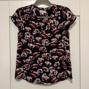 Kortärmad blus - Kortärmad blus från Bondelid. Marinblå med vinröda/vita blommönster. Storlek 36. Liten trådmaska som syns till vänster på sista bilden. 