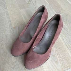 Mörkrosa pumps med glittrig klack och platåsula - Mörkrosa/gammelrosa pumps med glittrig klack och platåsula. Mockaimitation. Nyskick. Klackhöjd ca 8 cm. Storlek 37.  Mjuk sula invändigt. 