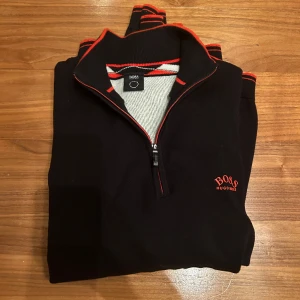 Hugo boss tröja - Säljer nu denna snygga halfzip från Hugo boss i enastående skick, 10/10. Svart med orangea detaljer. 