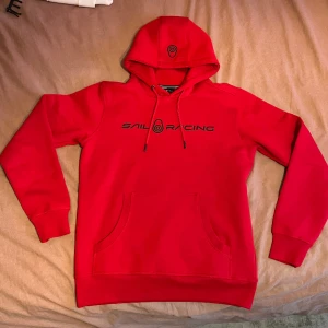 Röd Sailracing Hoodie - Säljer en helt ny Sailracing hoodie i röd färg med storlek S. Inte använd pågrund av att den är lite kort på mig. Nypris ligger på 1.200kr men kom med förslag då priset inte är  hugget. Mer info så tveka inte med att höra av dig 👍