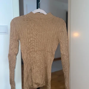 Kamelfärgad tröja med halvpolo. Slits i ärmarna. - En långärmad fin tröja med slits i ärmarna. Halvpolo. Storlek S.