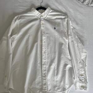 En Ralph Lauren skjorta i vit med mörkblå logga storlek L. En mindre brun fläck som jag inte vårdat med vanish men kan ha möjlighet att försvinna. Typisk sommarskjorta som är köpt under sommaren 2023z
