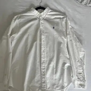 En Ralph Lauren skjorta i vit med mörkblå logga storlek L. En mindre brun fläck som jag inte vårdat med vanish men kan ha möjlighet att försvinna. Typisk sommarskjorta som är köpt under sommaren 2023z