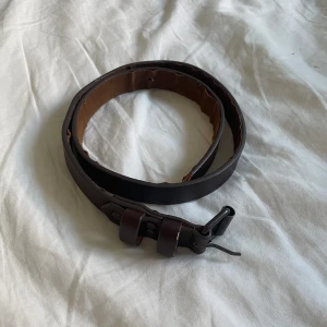 Brunt skärp  - Ett brunt, fint men gammalt skärp som passar bra till jeans! Skärpet är 74cm långt och ungefär 2cm brett. Insidan av skärpet är lite gammalt och har därför risken att ramla av om den slits för mycket! Annars är den i bra skick och ser nästan ny ut! 