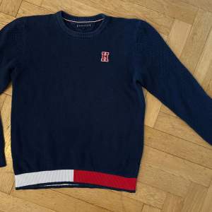 Stickad Tommy Hilfiger tröja i blått med vita och röda detaljer. Storleken som står på tröjan är 176 men stämmer ej, motsvarar mer en 164.
