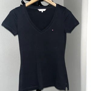 Tommy Hilfiger T-Shirt - Superfin svart t-shirt med v-ringning och slits nedtill från Tommy Hilfiger, storlek XS. Material 100% bomull. Endast använd ett par gånger, skick som ny!   Kan fraktas eller mötas upp i Göteborg.