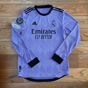 Real Madrid 22/23 bortaställ Champions League edition - Tja! Säljer nu denna tvär feta tröjan då den är för liten. Köpt på bernabeu där jag valde att köpa den för 2000kr. Tveka inte på att fråga ifall du har frågor🙏