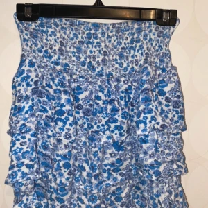 Söt blommig kjol - Söt blommig kjol från BikBok!  Kort kjol med volanger, vit och blå blommig ☺️ Storlek XS men väldigt stretching så passar även S, eventuellt M. Hör av er vid frågor eller fler bilder!