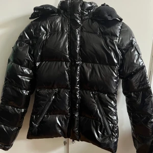 Glansig dunjacka - Svart glansig dunjacka från märket Wolffwear med ficka på ärmen. Nyskick, säljer pga för liten storlek.