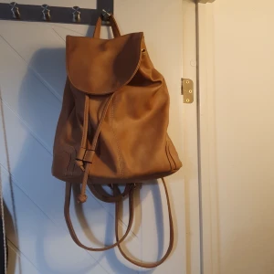Ryggsäck  - Lite mindre storlek på ryggsäck i gul-beige skinnimitation med snörning, knapp, fickor, dragkedja till både inner- och ytterfickor. 