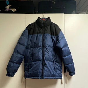 Pufferjacka  - Blå pufferjacka med svart detalj 🧿 Den varmaste jackan som finns till denna kalla vintern! 🥶Oversized fit, passar M-XXL👕Liknar North Face jackorna 🏂 Passed down oanvänd från farfar och använd endast gång då den är för stor på mig 💙 Utmärkt skick!