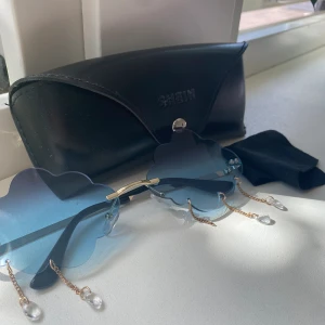 Ett par moln glasögon  - Ett par blåa solglasögon. En diamant har lossnat, annars i fint skick. Solglasfodralet får man med vid köpet.