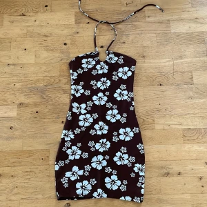Fin sommar klänning - Fin sommrig klänning. Trikå. Det sitter snören på framsidan som man knyter i nacken. Den är brun med vita hawaii blommor.