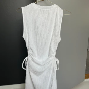 En vit klänning  - Super fin klänning som man kan knyta åt snören på sidorna av midjan!