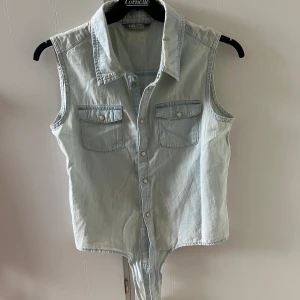 Tunn ärmlös jeansblus med knyt i midjan. - Tunn ärmlös jeansblus med knyt i midjan. St 164, passar XS Lindex