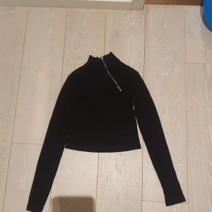 NA-KD En svart ribbad tröja med en dragkedja som går diagonalt ner till bröstet. - Storlek XS.