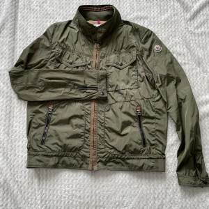 Moncler Field Jacket - Jacka från Moncler. Äldre modell med certilogo. Jackan är water-repellent. Storleken är 6 men sitter som L. Skicket är riktigt bra! Dock en liten skavank på ryggen. Skriv om funderingar eller fler bilder!