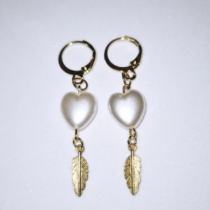 Vitt hjärta med fjäder  - Ej äkta guld örhängen( kan innehålla nickel), guldig fjäder (ej äkta), vitt akryl hjärta. 