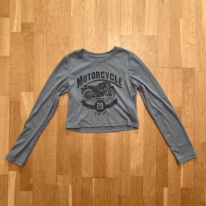 Blågrå, långärmad croptop i ribbat, stl S - Croppad långärmad topp med en motorcykel på. Tröjan är enbart använd fåtal gånger och är i stl S. Klicka gärna på köp nu och meddela för eventuella frågor. :)