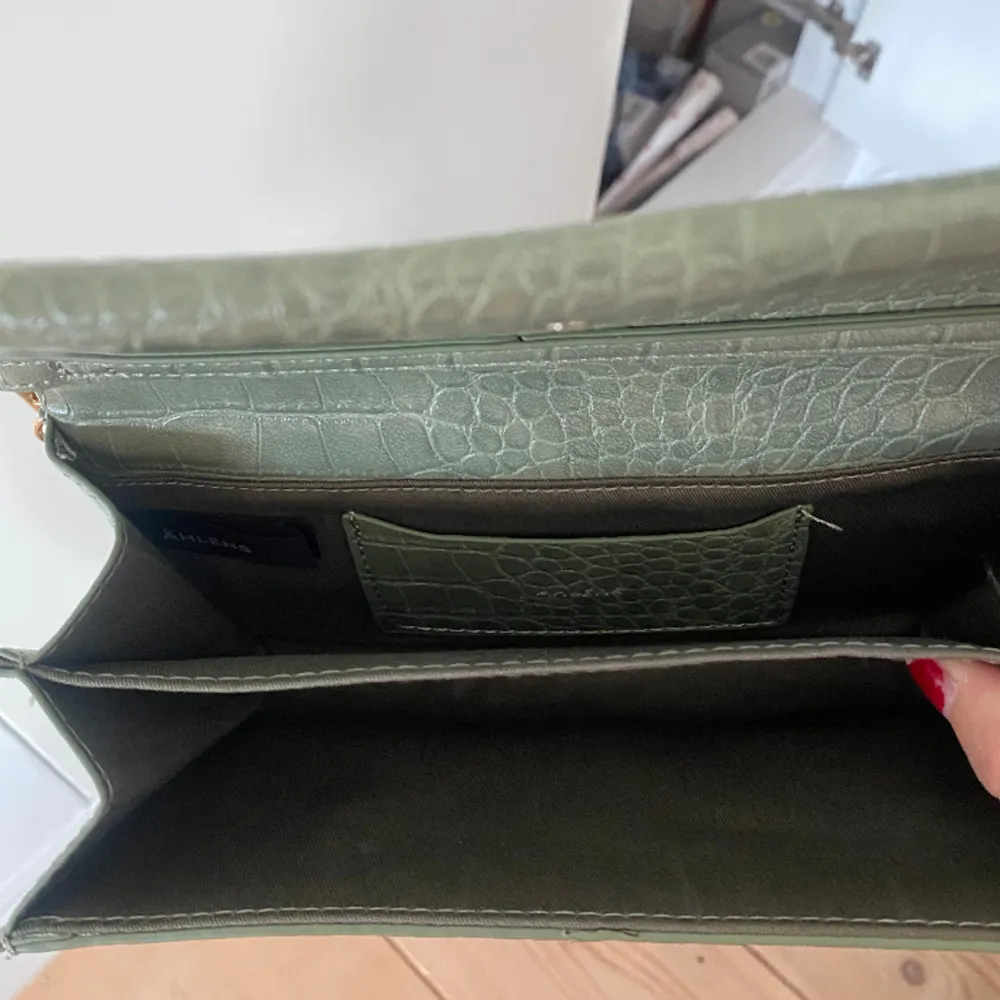 En grön väska från Åhléns. Man kan ha väskan över axeln som en pochette väska, men man kan även ta av bandet och ha väskan som en kuvertcäska. Köparen Står för frakten, inga returer 🥰. Väskor.