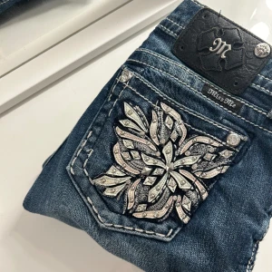 MissMe jeans Bootcut - Miss Me Jeans, Signature Boot Cut, Low Rise, Rodeo Thick Stitch, Storlek 25x30.  Väldigt bra skick men saknar tre nitar bak på märkeslappen (se bild). Byxorna är uppsydda till 30 tums längd.