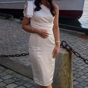 Vit knälång klänning från Boohoo - Använd endast 1 gång. Kommer ca till knäna och är en one shoulder kläning med en hängande volang på ena axeln. Den är i satin. 