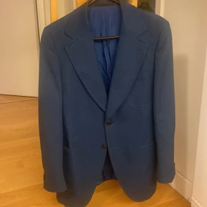 Marinblå enkelknäppt kavaj  - Kavaj i superskick. Inga defekter förekommer. Breda, trubbiga slag.  Ärmlängd: 63,5 cm Axel-axel: 44 cm Längd (rygg): 76 cm Midja: 96 cm