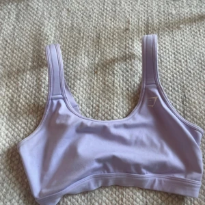 Ljuslila sporttopp från Gymshark - En ljuslila sporttopp från Gymshark med breda axelband och en tight passform. Toppen är tillverkad i ett elastiskt material som ger bra stöd under träning.