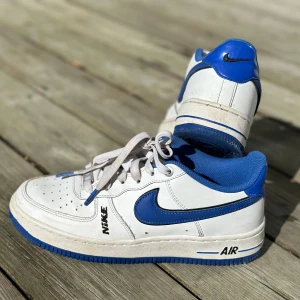 Nike Air Force LV8 vit/blå - Låg vit/blå läder sneaker med stötdämpande Air mellansula, vadderad ankelparti och Nike logga.  Använd under 10 gånger 