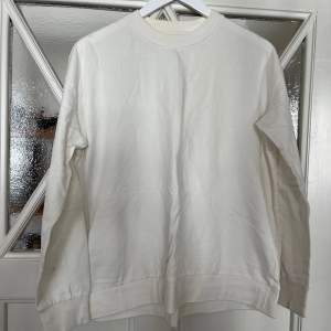 En vit långärmad tröja från 157 i storlek M. Tröjan har en enkel design med ribbstickade muddar vid ärmslut och nederkant. Den är i välanvänt skick med synliga fläckar.