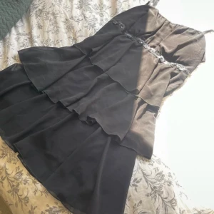 Svart klänning med volanger - En jättefin svart klänning med volanger och en flätad paljettdetalj, den passar till alla tillfällen och är i nyskick. Den är i storlek S/M