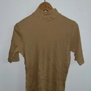 Beige kortärmad minipolo  - En beige tröja med minipolokrage, tröjan är ganska stretchig så passar både M-XL beroende på vilken passform man vill ha, den andra bilden är passformen på mig som har strl L. 