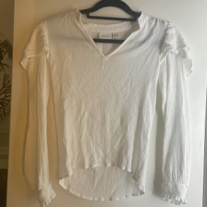 Blus  - Materialet är tunt och stretchigt, blusen har volanger på axlarna och en V ringning vi halsen