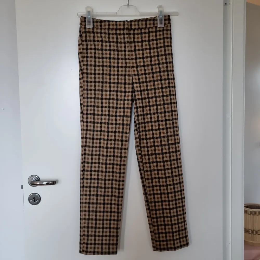Ett par snygga bruna byxor med rutigt mönster. Tyget är mjukt och bekvämt. De har ganska små fickor på framsidan och fickorna på baksidan är fake. Nypris: 599 kr. Jeans & Byxor.